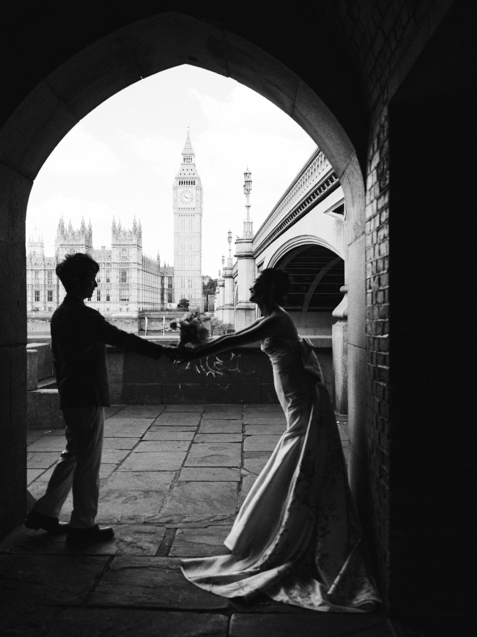 A black-and-white wedding portrait under a London arch